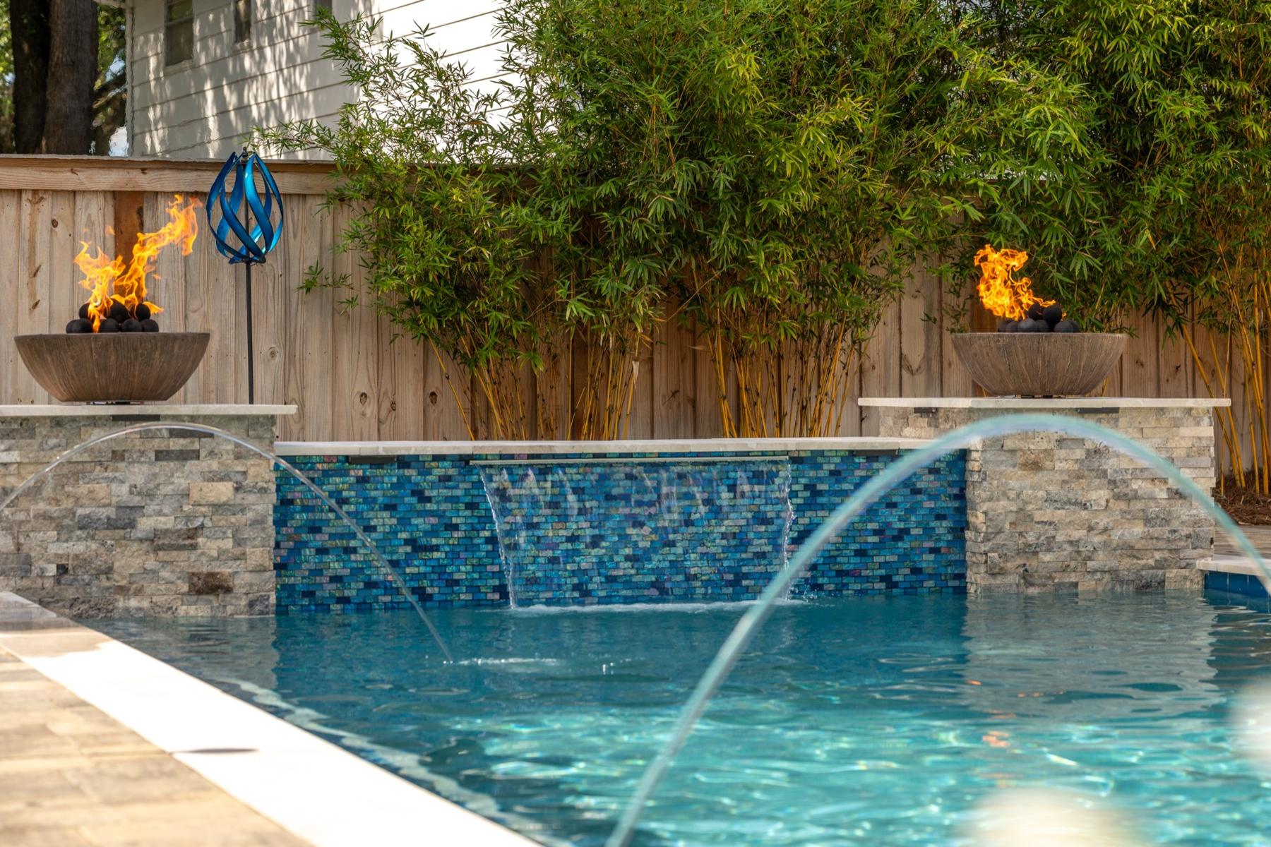 Glass-tile spillway wall with fire bowls and deck jets on a Breakwater pool